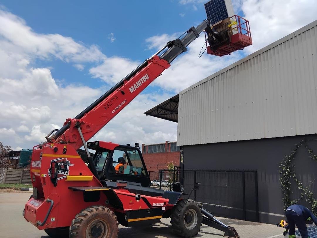 Manitou telehandler on hire in Harare lifting a solar panel to a roof in the work basket
